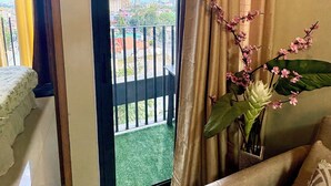 Una habitación con balcón, cama, sofá y un jarrón con flores.