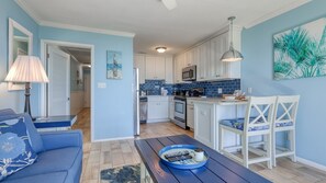 Eine moderne Küche mit weißen Schränken, einer Mikrowelle und einer blauen Spritzschutzwand. Es gibt einen Essbereich mit einem blauen Sofa und einem Tisch mit einer blauen Schüssel.