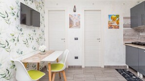 A modern kitchen with a flat-screen TV, a dining table with chairs, and two doors with artwork.