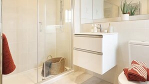 Ein modernes Badezimmer mit Duschkabine aus Glas, einem weißen Waschtisch mit Spiegel und einer Toilette.