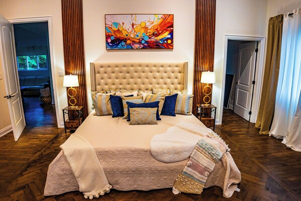 Une chambre à coucher avec un grand lit, une tête de lit, deux tables de chevet et un tableau abstrait aux couleurs vives accroché au mur.