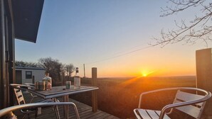Terassi, jossa on tuoleja ja pöytä, ja josta avautuu näkymä auringonlaskuun.