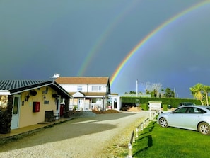 A residential area with houses, a car, and a visible rainbow. - Elizabeth Carne (No Man's Land)