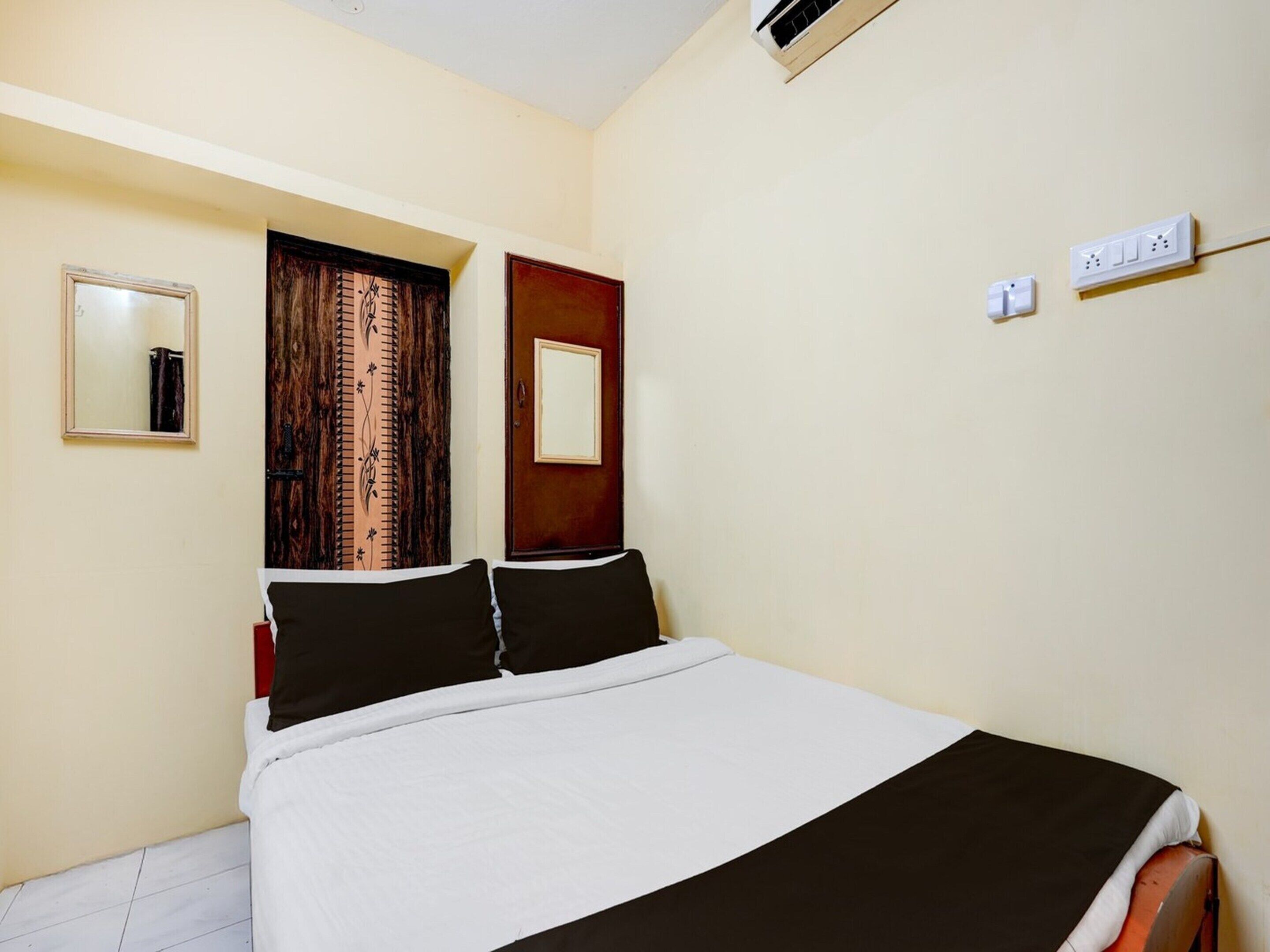 A hotel room with a bed, a mirror, a door, and a wall-mounted air conditioner.