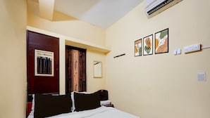 A hotel room with a bed, a door with a curtain, a wall-mounted air conditioner, and three framed pictures. - Deluxenimalan Residency (Chennai)