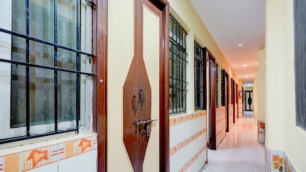 A hotel corridor with multiple doors, tiled walls, and windows with metal bars. - Deluxenimalan Residency (Chennai)