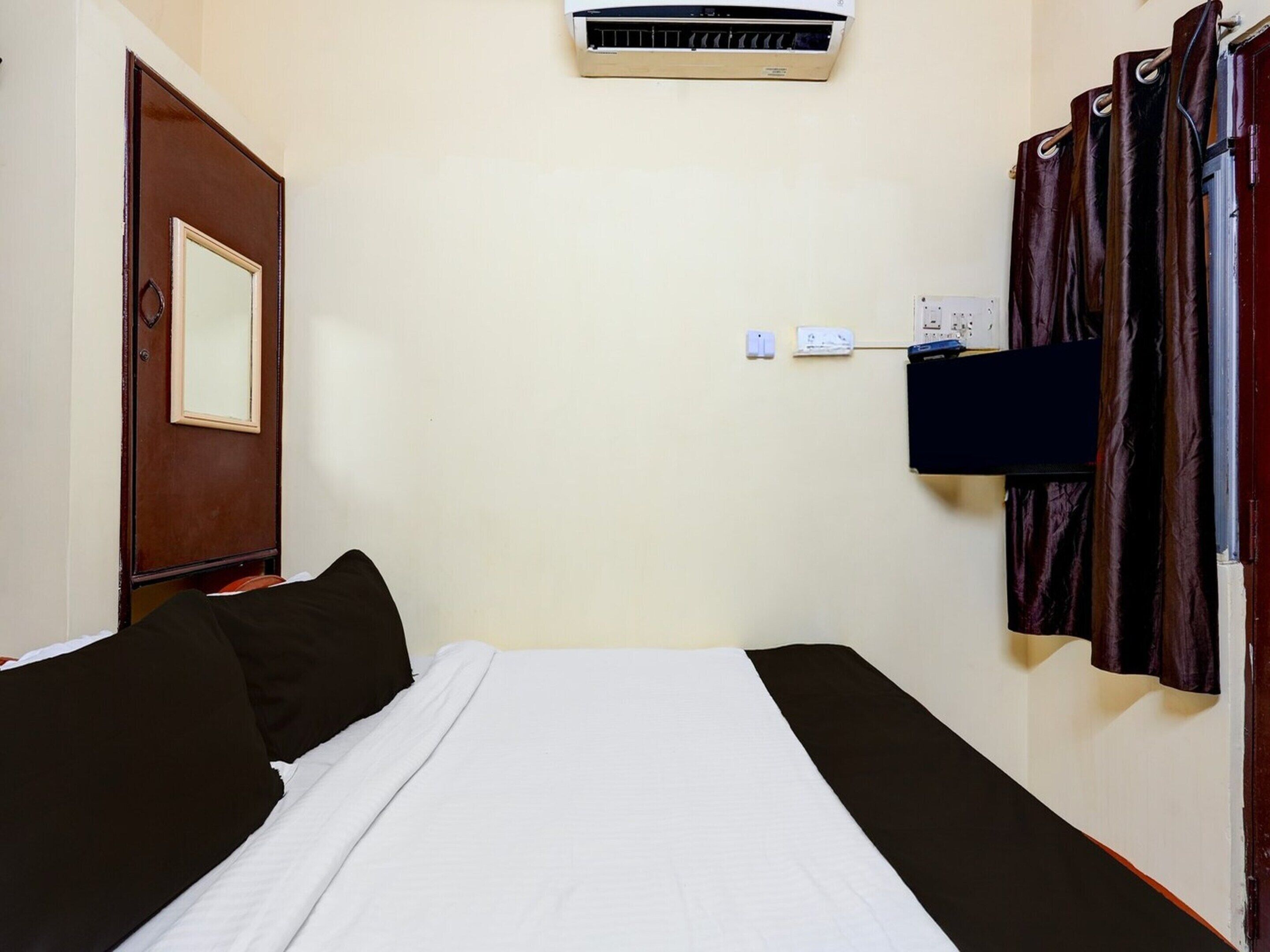 A hotel room with a bed, an air conditioning unit, a television, and a curtain.