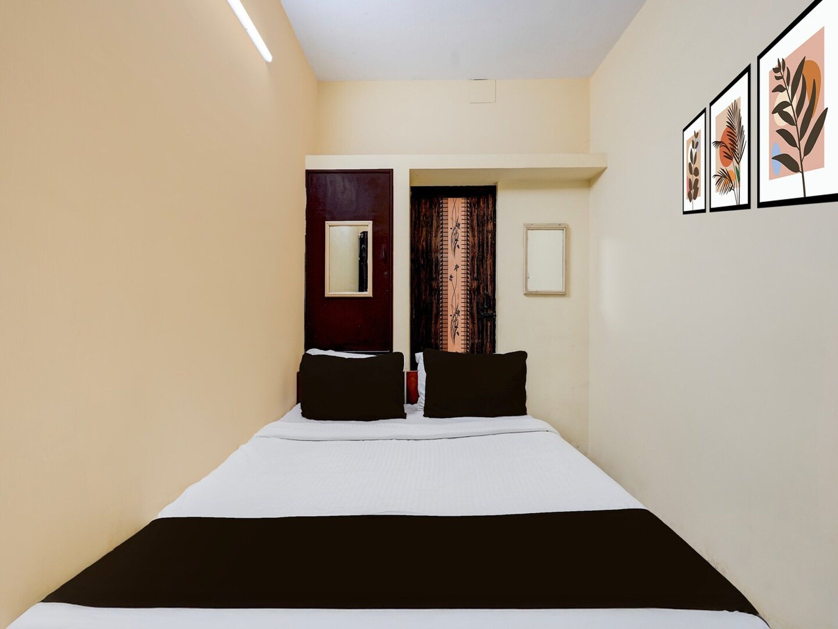 Une chambre d’hôtel avec un lit, une porte, un miroir et des œuvres d’art encadrées accrochées au mur.