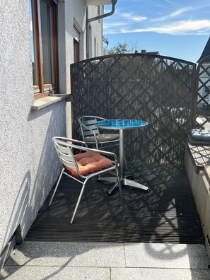 Une petite terrasse extérieure avec une table et deux chaises, une terrasse en bois et un mur blanc.