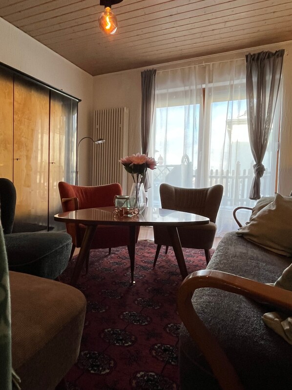 Un salon avec une table ronde, deux chaises, un canapé, un radiateur et une fenêtre avec des rideaux.