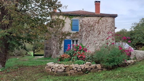 A stone house with a red car parked nearby, surrounded by a garden with various plants and flowers. - maison d'hôtes Lacour (Augignac)