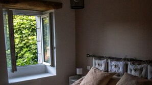A bedroom with a large bed, a window with a view of greenery, a bedside table with a lamp, and a ceiling fan. - maison d'hôtes Lacour (Augignac)