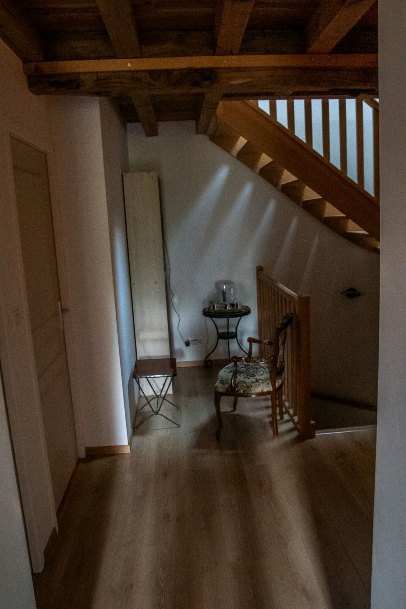 Ein schmaler Flur mit Holzboden, einem kleinen Tisch mit Stuhl, einem Heizkörper und einer Treppe mit Holzwangen.