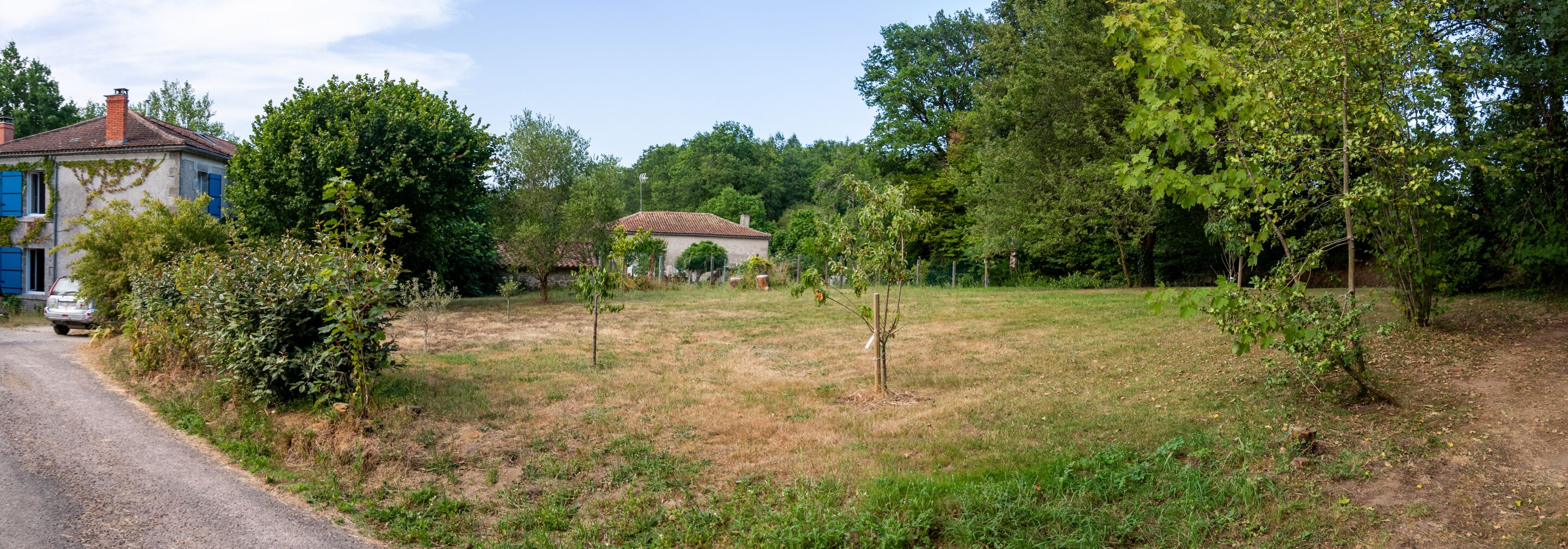 A rural setting with a gravel road, a house with blue shutters, and a small building in the background.