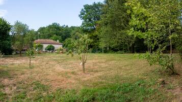 A rural setting with a gravel road, a house with blue shutters, and a small building in the background.