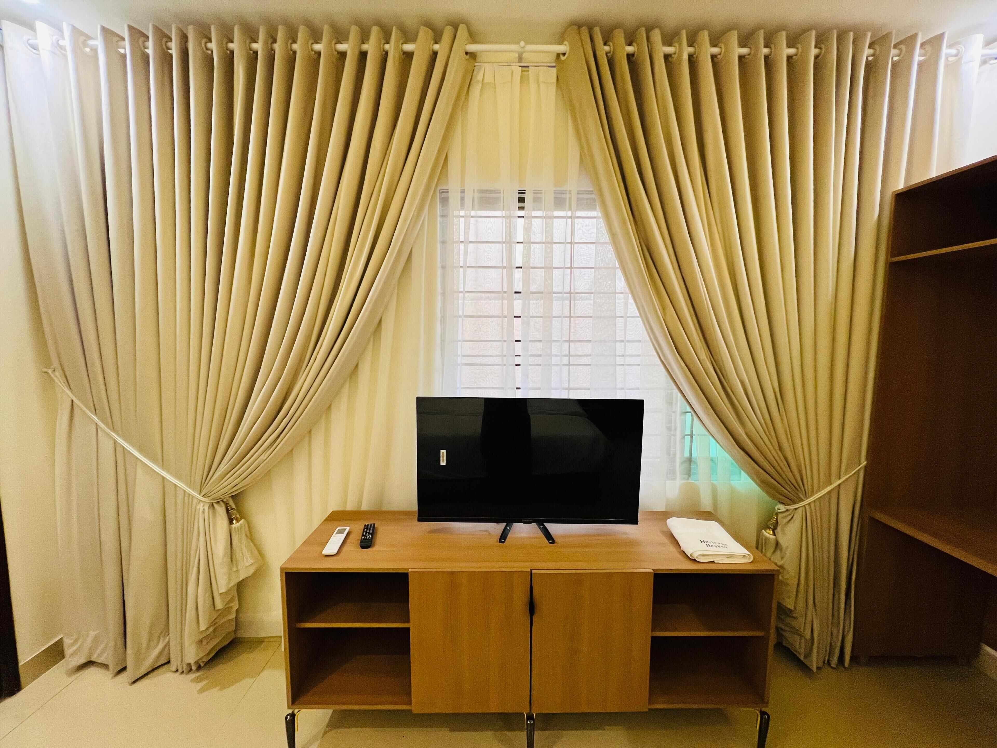 A room with a TV on a wooden stand, a remote control, and a folded towel on the stand.