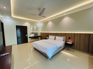 A modern bedroom with a large bed, a ceiling fan, recessed lighting, a wooden headboard, and a nightstand with a lamp. - Heritage Heaven (Karachi)