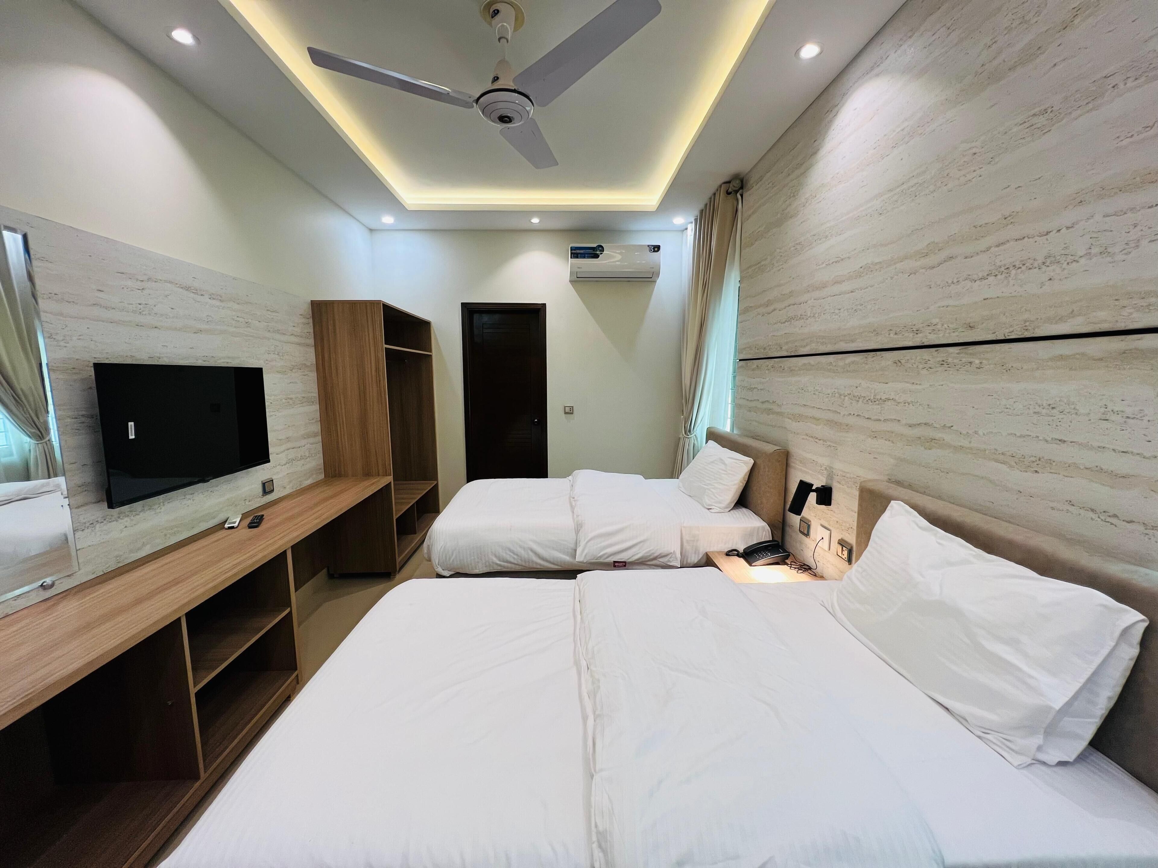 A hotel room with a flat-screen TV, two beds, a ceiling fan, and built-in wardrobes.