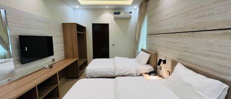 A hotel room with a flat-screen TV, two beds, a ceiling fan, and built-in wardrobes.