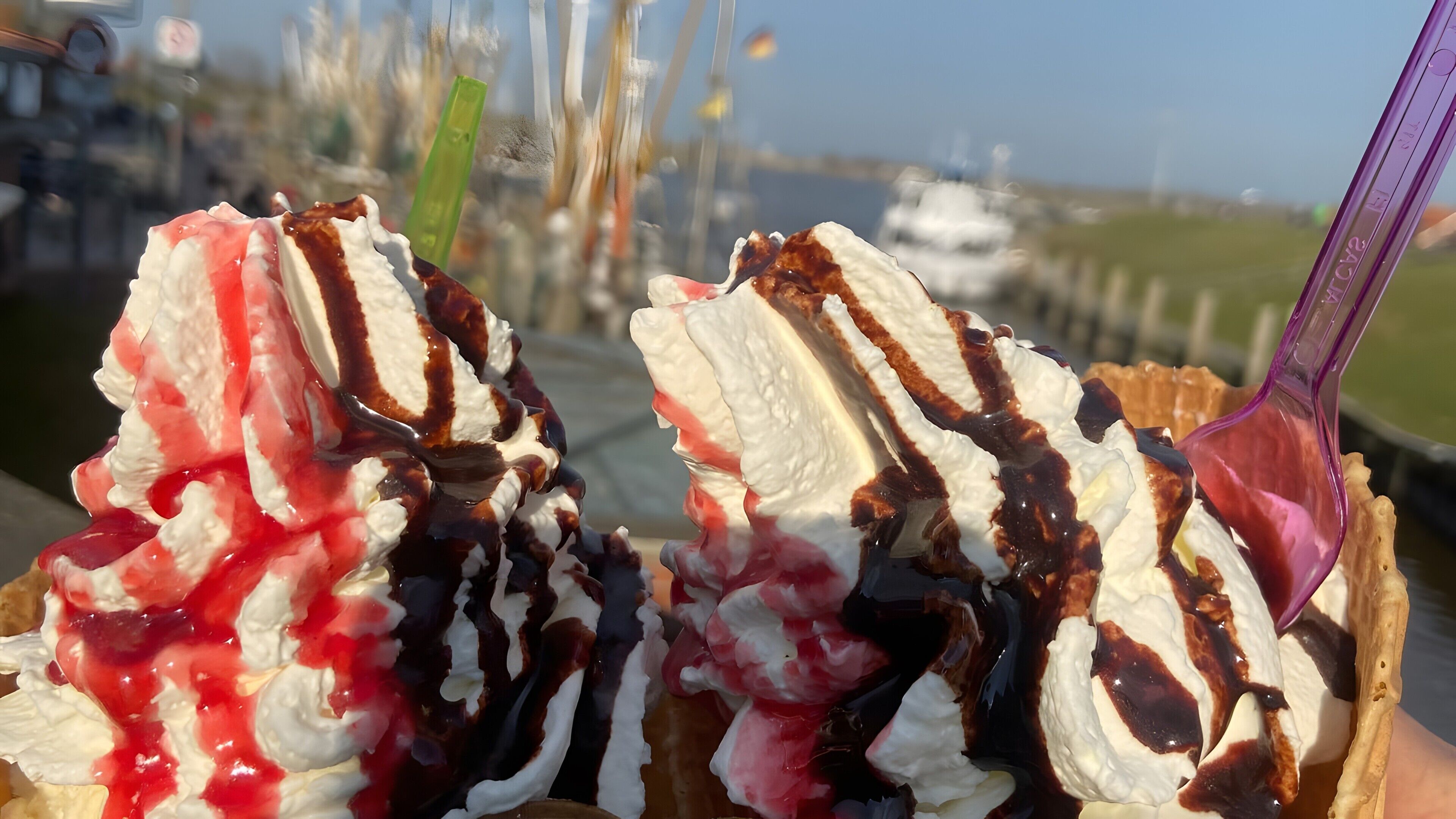 A close-up of a dessert with whipped cream, chocolate syrup, and red fruit topping.