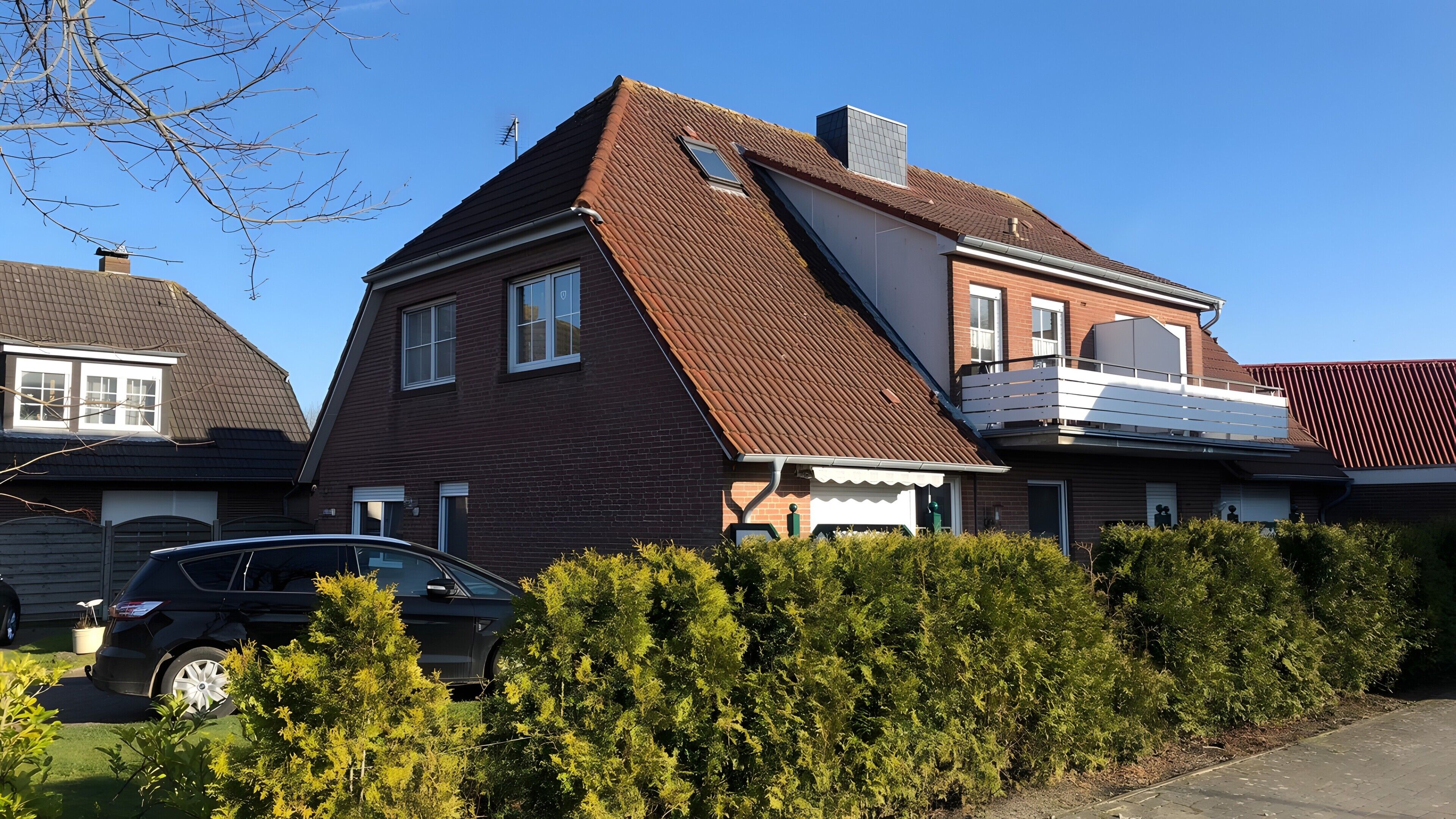 Ein zweistöckiges Haus mit geneigtem Dach, einem sichtbaren Schornstein und einem Auto auf der Auffahrt.