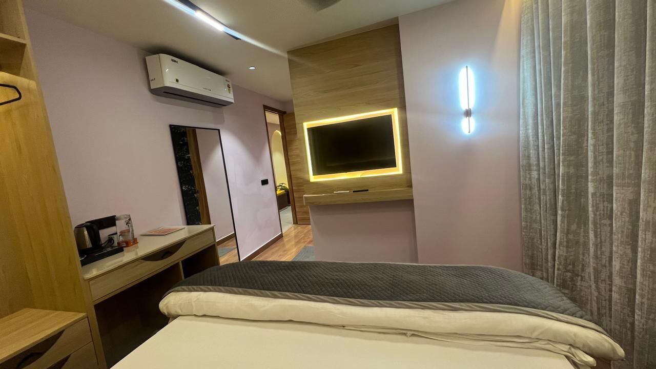 A hotel room with a bed, a desk, a mirror, an air conditioning unit, a television, and a curtain.