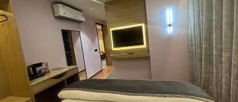 A hotel room with a bed, a desk, a mirror, an air conditioning unit, a television, and a curtain.