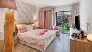 Ein Schlafzimmer mit einem großen Bett, Nachttischlampen, einem Fernseher, einem Schreibtisch mit Lampe und Blick auf einen Garten durch eine Schiebetür.