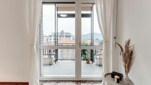 A room with a large sliding glass door leading to a balcony with a city view. - Ruan Downtown (Como)