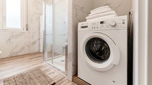 A modern bathroom with a built-in washing machine, a glass shower enclosure, and a marble-tiled wall. - Ruan Downtown (Como)