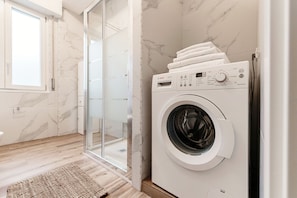 Ein modernes Badezimmer mit integrierter Waschmaschine, einer Duschkabine aus Glas und einer Wand mit Marmorplatten.