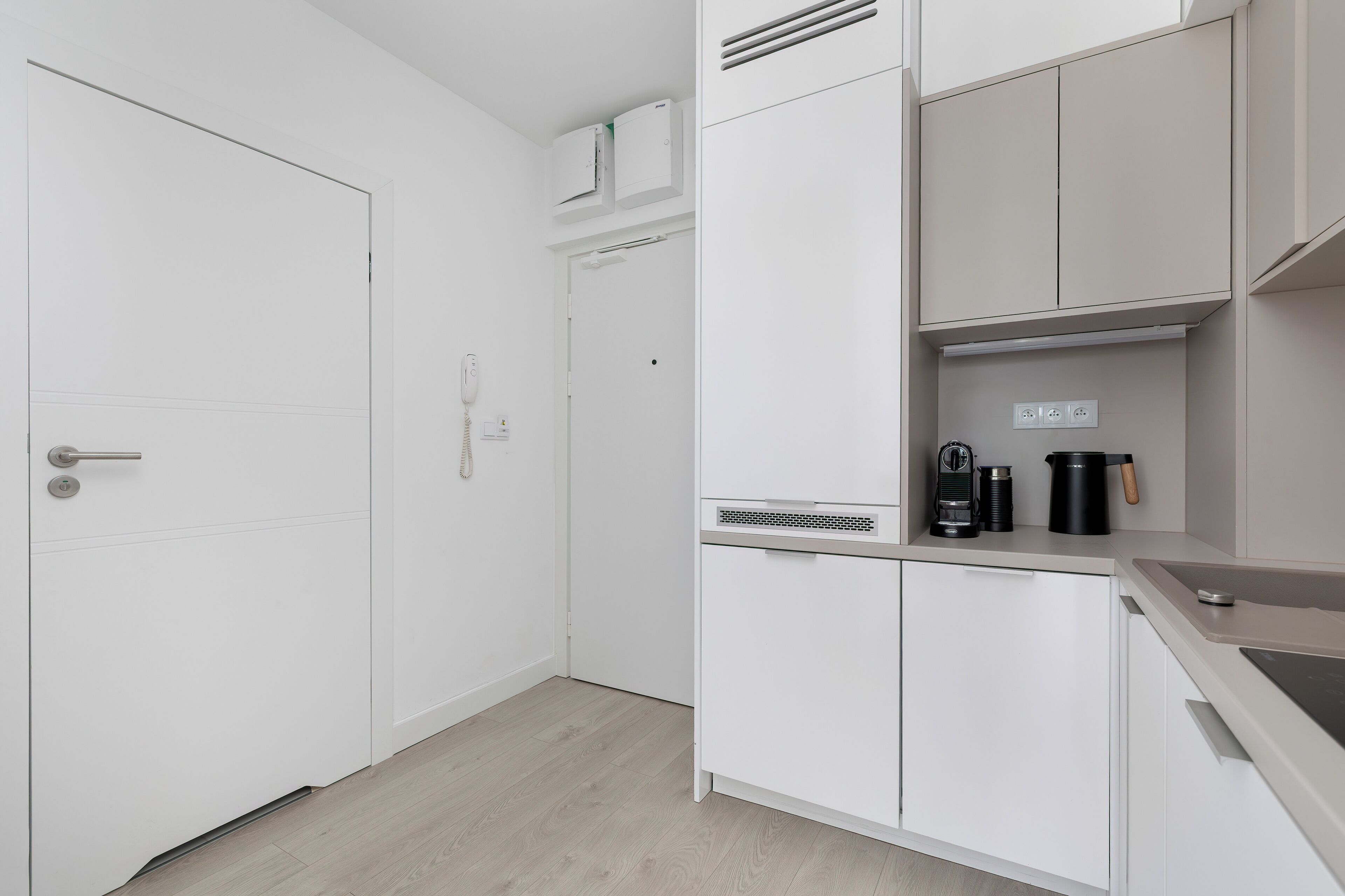 Une cuisine moderne avec des meubles blancs, un four encastré et une machine à café posée sur le plan de travail.