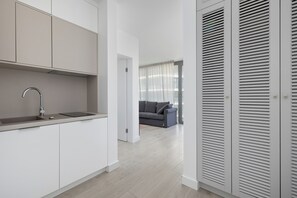 Eine moderne Küche mit weißen Schränken, einer Edelstahl-Spüle und einem grauen Sofa im Wohnbereich.