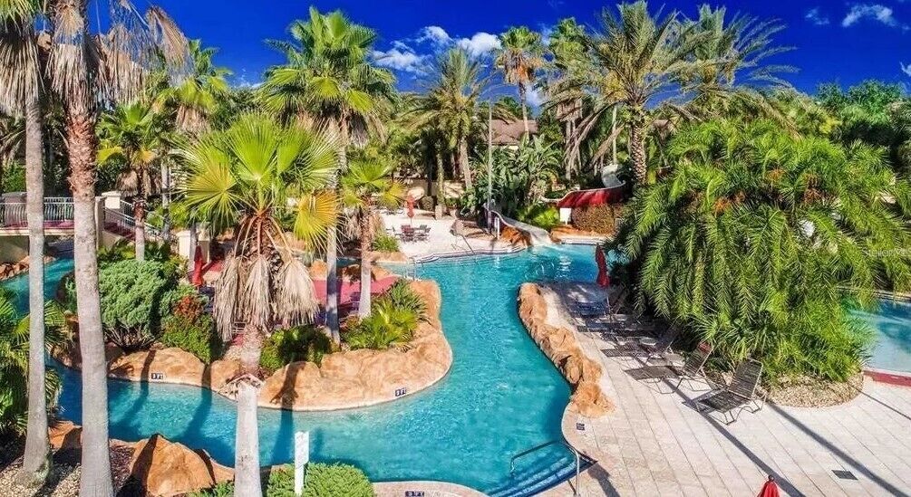 A pool area with palm trees, lounge chairs, and a water slide.