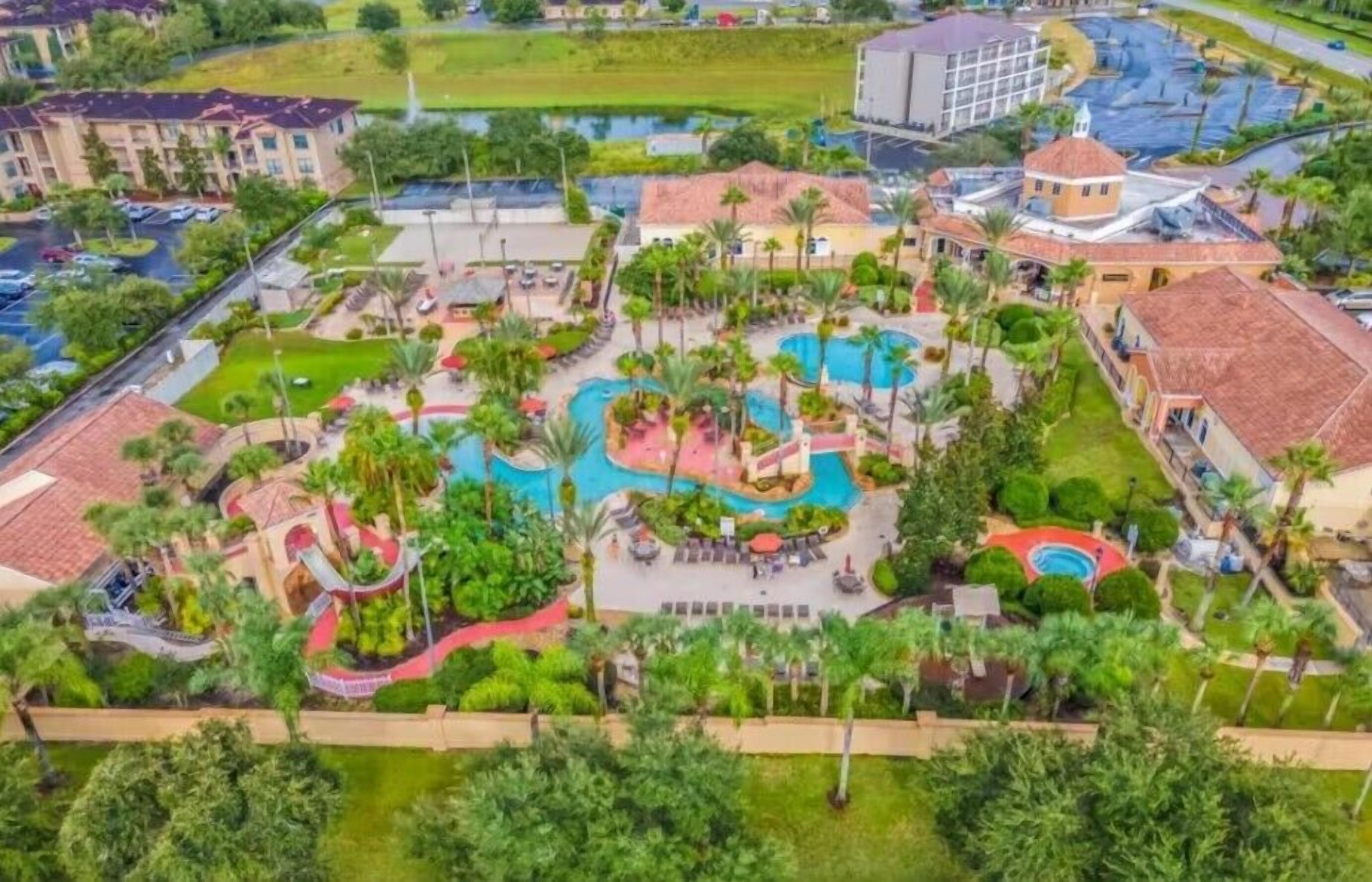 Vista aérea de un resort con varias piscinas, palmeras y un edificio central con techo rojo.