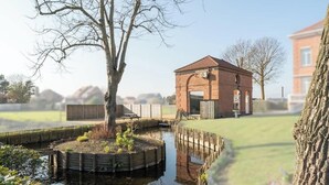 Un bâtiment en briques avec un toit rouge, une clôture en bois et un arbre au premier plan.