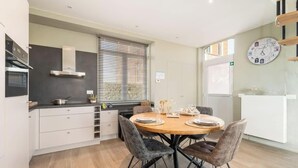 Une cuisine moderne avec une table à manger, des chaises, une horloge et une fenêtre avec des stores.