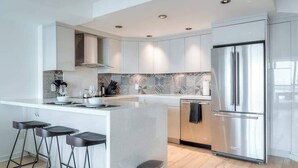 Una cocina moderna con armarios blancos, un refrigerador de acero inoxidable y una isla central con taburetes de bar.