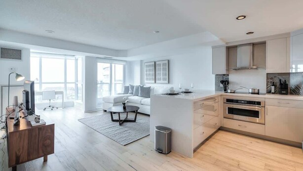 Una cocina moderna con una isla central, horno empotrado y una zona de comedor con sofá y mesa de centro.