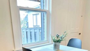 A dining area with a white table and black chairs, a window with a view of buildings, and a potted plant on the table.