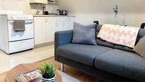 Una cocina moderna con armarios blancos, una estufa blanca y un sofá gris con una manta estampada.