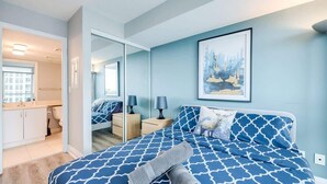 Un dormitorio con cama, una mesita de noche, una lámpara, un espejo y un cuadro en la pared.