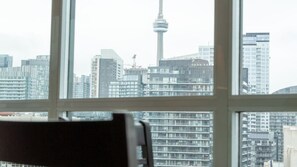A view through a window of a cityscape with high-rise buildings and a prominent tower. - CN Tower Views • 2BR+Den Condo w/ Parking (Toronto)