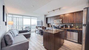 A modern kitchen with dark wood cabinets, stainless steel appliances, and a granite countertop island. - CN Tower Views • 2BR+Den Condo w/ Parking (Toronto)