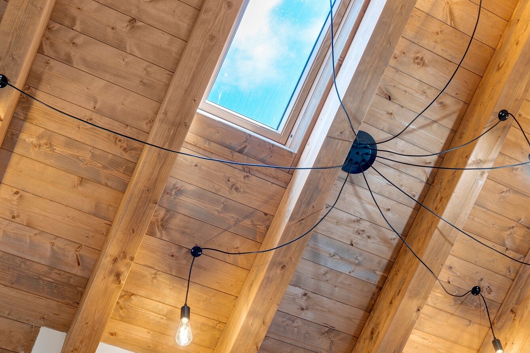 Een houten plafond met zichtbare balken, een dakraam en hanglampen.