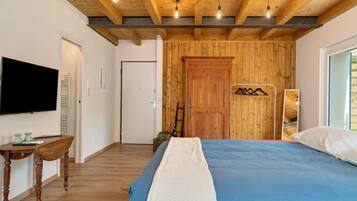 Ein Schlafzimmer mit Holzbalkendecke, einem Bett mit blauer Bettdecke, einer weißen Decke, einem Holzschrank und einem Fernseher an der Wand.