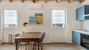 A dining area with a wooden table and chairs, a kitchen with blue cabinets, and artwork on the wall. - Studio Apartment with Garden (Rossiglione)