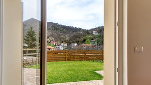 A view through a glass door to a backyard with a wooden fence, a paved patio, and houses in the background. - Studio Apartment with Garden (Rossiglione)