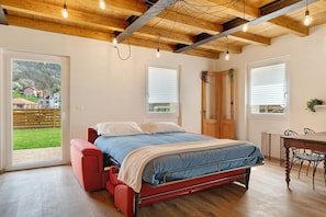 Un dormitorio con una cama, techo de madera y vista a un paisaje verde a través de una puerta.