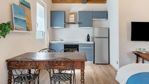 A compact kitchen with modern appliances, a dining table with chairs, and a flat-screen TV mounted on the wall. - Studio Apartment with Garden (Rossiglione)
